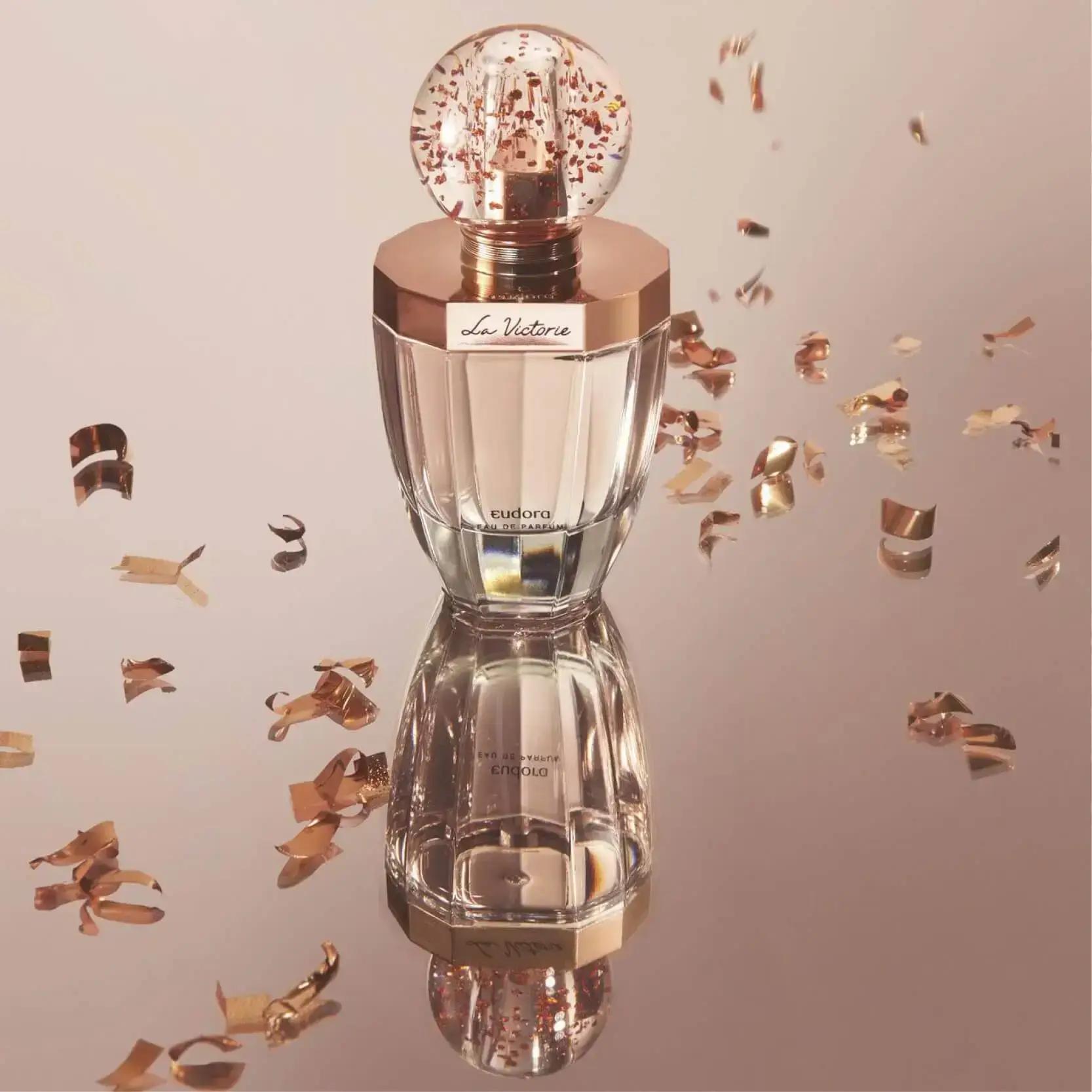Perfume La Victorie com vidro e detalhes em cobre, no fundo cor de cobre e raspas de cobre.